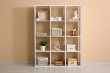 Bej duvarın yanında dekorasyonu olan raf ünitesi.