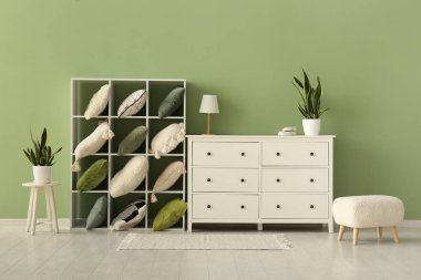 Yastıklı ve çekmeceli raf ünitesi yeşil duvarın yanında.