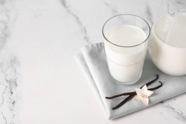 Bir bardak taze vanilya sütüyle çubuklu ve çiçekli beyaz arka plan