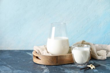 Bir bardak taze vanilya sütü, çubuklu ve mavi arka planda çiçek.