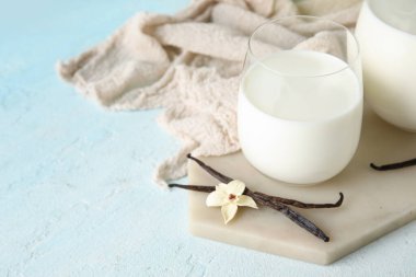 Bir bardak taze vanilyalı süt ve açık mavi arka planda çiçek.