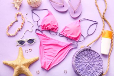 Composition with stylish female swimsuit and beach accessories on lilac background