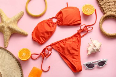 Şık kadın mayoları, plaj aksesuarları ve pembe arka planda turuncu renkte kompozisyon