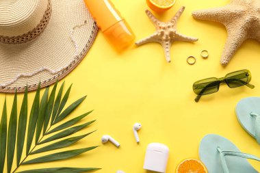 Şık plaj aksesuarları, kulaklıklar ve sarı arka planda palmiye yaprağından yapılmış çerçeve.