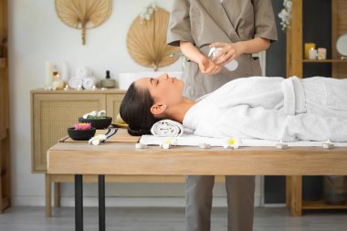 Terapist, kaplıcada genç bir bayana masaj yapmadan önce krem sürüyor.