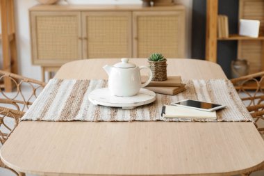 Tablet bilgisayarlı çaydanlık ve yemek masasında kitaplar.