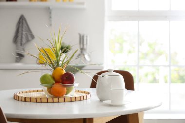 Mutfaktaki yemek masasında bir fincan kahve ve meyveli çaydanlık.