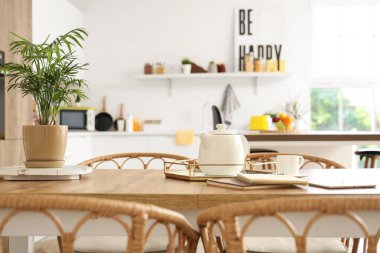 Mutfaktaki yemek masasında defterleri ve tablet bilgisayarı olan bir çaydanlık.