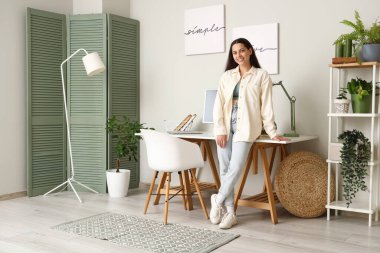 Masanın üstündeki ışık duvarına posterler asan genç bir kadın.