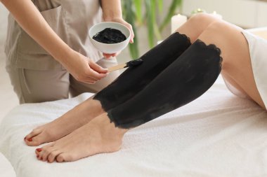 Masaj terapisti spa salonunda kadının bacağına çamur sürüyor.