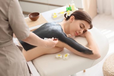 Masaj terapisti spa salonunda kadının sırtına çamur sürüyor.