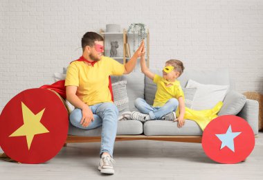 Süper kahraman kostümü giymiş babasıyla küçük bir çocuk evde birbirine beşlik çakıyor.