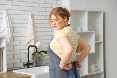 Mutfakta önlük bağlayan genç bir kadın.