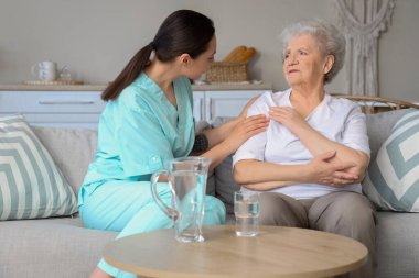 Fizyoterapist evde yaşlı bir kadını sakinleştiriyor.