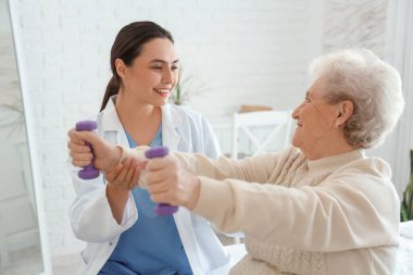 Fizyoterapist ve yaşlı kadın yatak odasında dambıllarla antrenman yapıyor.