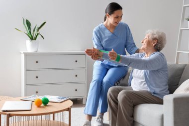 Evde esneme bandı ve fizyoterapisti olan yaşlı bir kadın var.