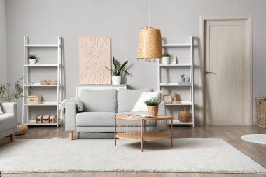 Gri kanepe, masa ve raf üniteleriyle aydınlık oturma odasının içinde.