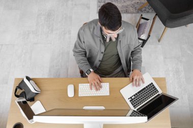 Ofiste bilgisayar ve dizüstü bilgisayar kullanan genç adam, üst görünüm