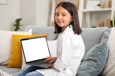Evdeki kanepede dizüstü bilgisayar kullanan küçük Asyalı kız.
