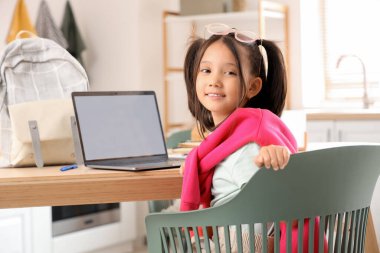 Bilgisayarlı küçük Asyalı kız mutfakta internetten ders çalışıyor.