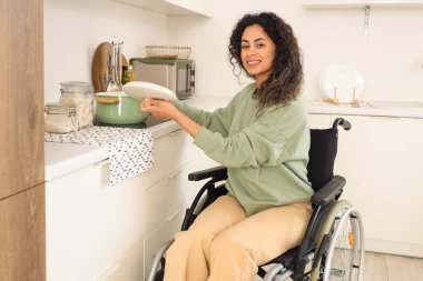 Tekerlekli sandalyedeki genç Afro-Amerikalı kadın evde elektrikli ocakta yemek pişiriyor.