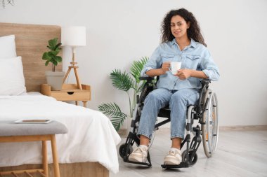 Tekerlekli sandalyedeki genç Afro-Amerikalı kadın evinde bir fincan kahveyle