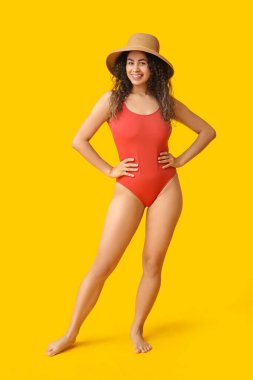 Şık kırmızı mayo ve sarı arka planda hasır şapkalı güzel Afro-Amerikan kadın.