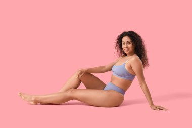 Pembe arka planda oturan şık iç çamaşırlı güzel, mutlu, Afro-Amerikan kadın.