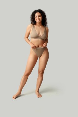 Gri arka planda şık iç çamaşırlı güzel, mutlu, Afro-Amerikan kadın.