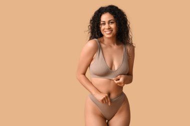 Güzel, mutlu, bej arka planda iç çamaşırlı Afro-Amerikan kadın.