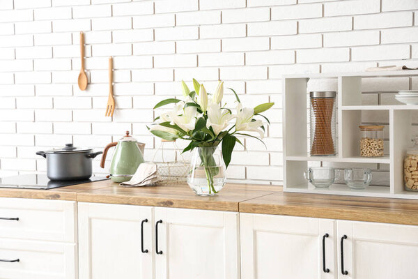 Ваза с красивыми цветами лилии на деревянном прилавке на кухне