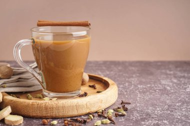 Grunge masasında farklı baharatlar bulunan bir bardak lezzetli masala çayı, yakın plan.