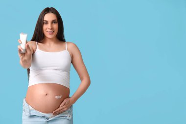 Genç hamile bir kadın krem sürmüş mavi arka planda çatlaklar var.
