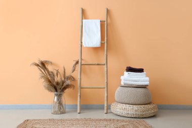 Poufs, merdiven ve vazo üzerinde temiz yumuşak havlu yığını. Turuncu duvarın yanında pampass otları var.