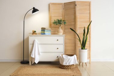 Beyaz duvarın yanındaki beyaz çekmecelerde yeşil dallı temiz havlu ve vazo yığını.