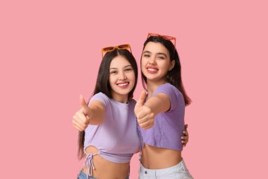 Güzel genç kadınlar pembe arka planda baş parmak hareketi yapıyorlar. Yaz partisi