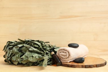 Meşe saunası süpürgesi, temel yağ, havlu ve ahşap zemin üzerindeki spa taşları.