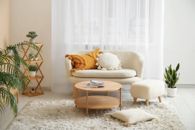 Beyaz kanepesi, sehpası, çekmeceleri ve perdeleri olan açık renk oturma odası.