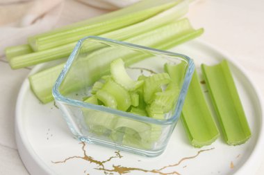 Beyaz ahşap zemin üzerinde taze yeşil kereviz kesilmiş tabak ve cam kase.