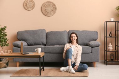 Şık bir oturma odasında, kanepenin yanında oturan genç bir kadın.