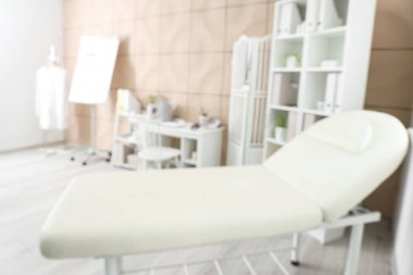 Kanepesi, doktor çalışma yeri ve raf üniteleri olan bulanık tıbbi ofis manzarası.