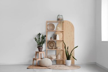 Odada beyaz duvarın yanında heykelcikli raflar ve bitkiler var.