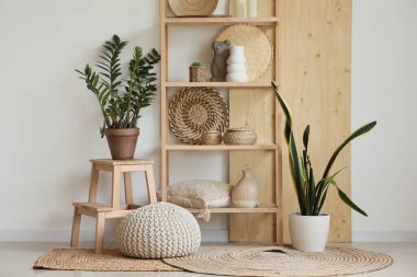 Odada beyaz duvarın yanında heykelcikli raflar ve bitkiler var.