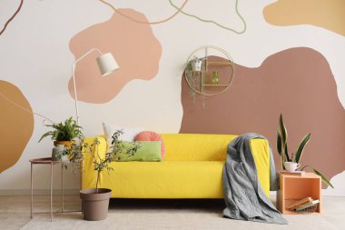 Sarı kanepesi, rafı, sehpası ve çiçekleri olan şık bir oturma odası.