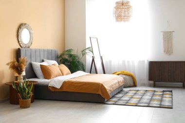 Rahat yatak, ayna ve vazo, güzel yatak odasındaki komodinin üzerinde otlar.