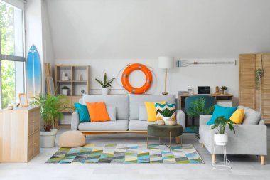 Oturma odasının içinde rahat koltuklar, puf ve sörf tahtası.