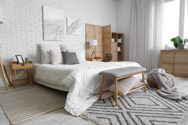 Стильный интерьер светлой спальни с большой удобной кроватью, деревянным складным экраном и скамейкой