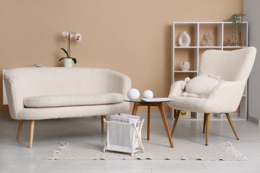 Oturma odasındaki beyaz kanepenin yanında dergilerle dolu bir depo sepeti.