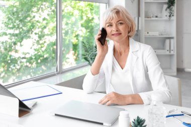 Klinikteki masada cep telefonuyla konuşan kadın doktor.