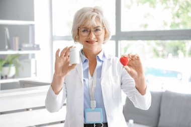 Klinikteki resepsiyon masasının yanında ilaç şişesi ve kalbi olan bir kadın doktor.